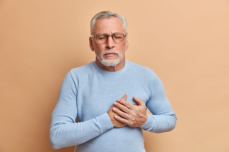 grey-haired-displeased-bearded-old-man-has-sudden-painful-spasm-in-chest-closes-eyes-and-presses-hands-to-heart-poses-against-beige-wall.png