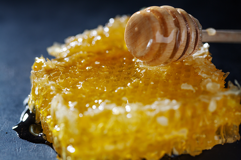 honeycombs-with-fresh-honey-and-honey-spoon-on-dark-background.png